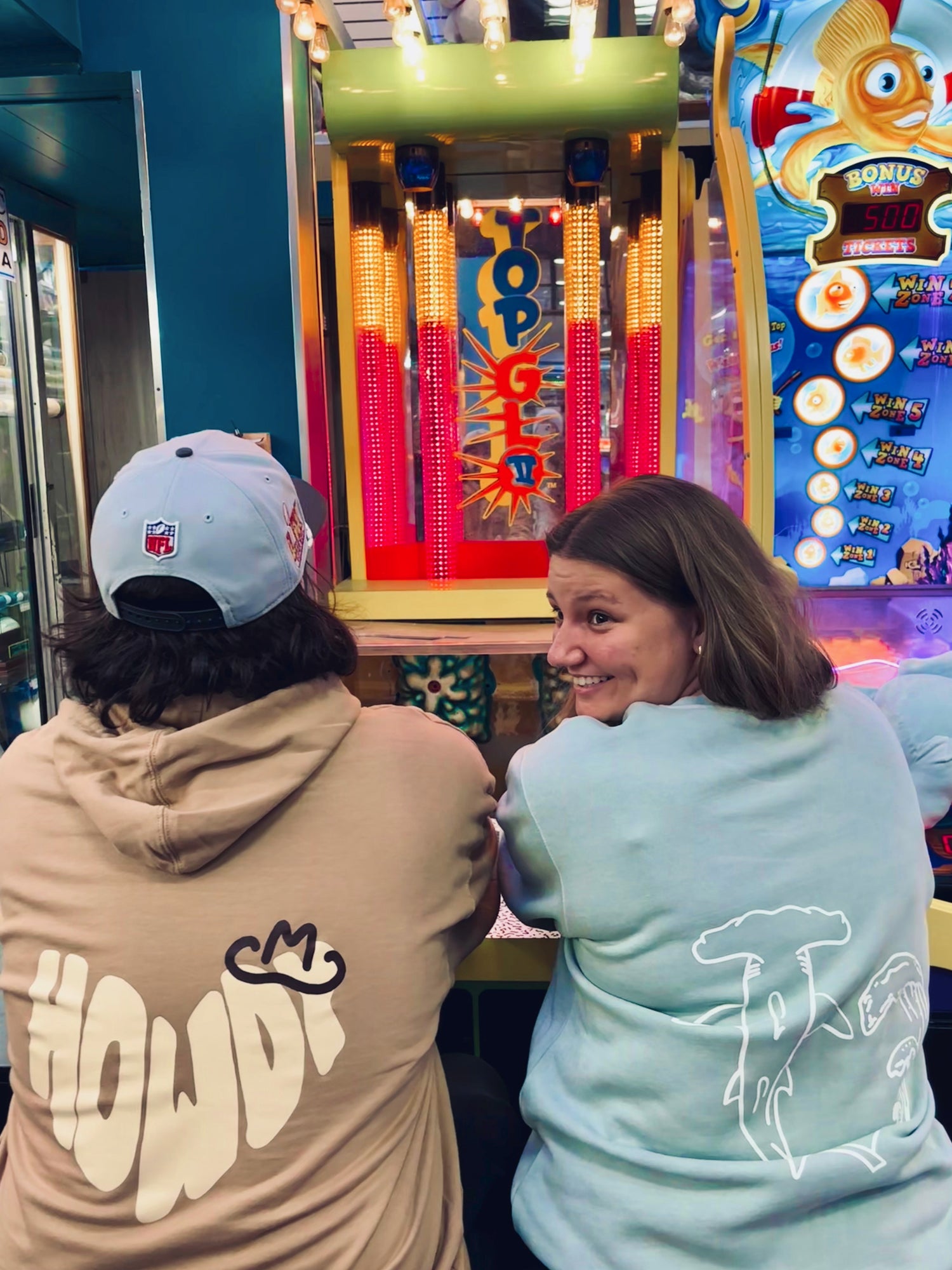 Two people playing a video game at an arcade with colorful screens and bright lights.